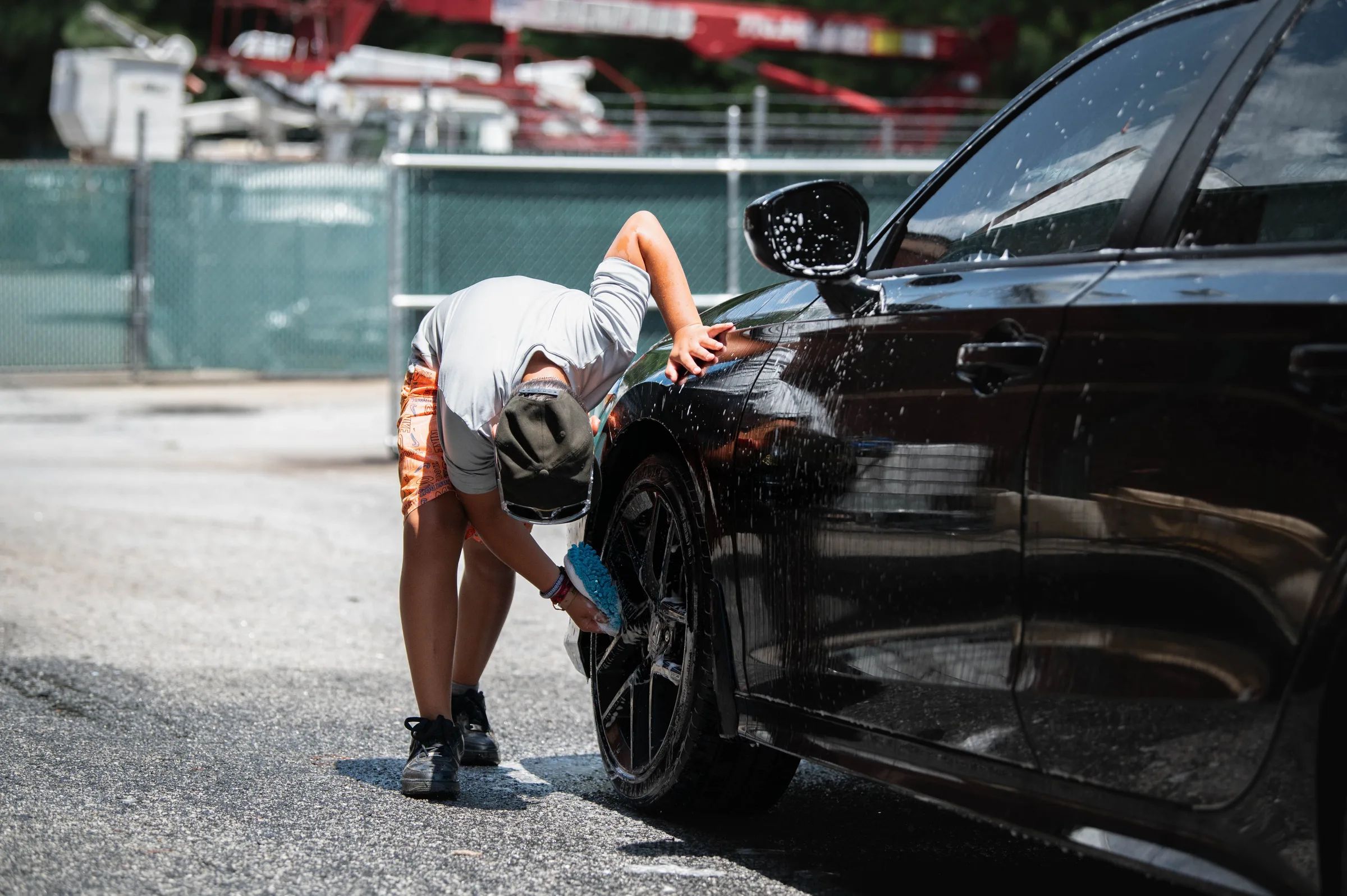 A person hand-cleaning the wheel of a black car outdoors
